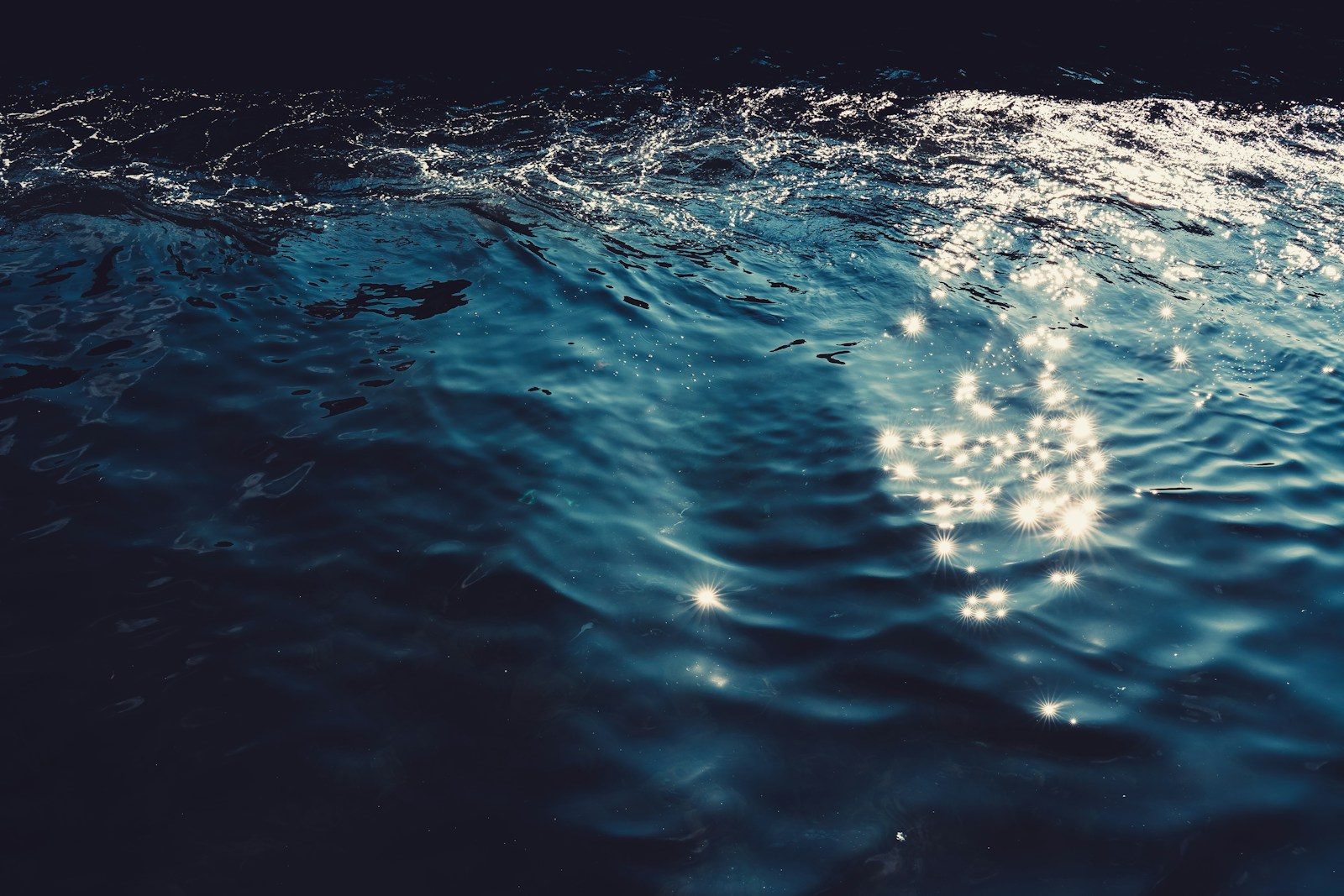 Dark blue ocean waves with sparkling sunlight reflections.